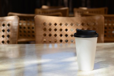 Photo of Takeaway coffee cup on beige table in cafe, space for text