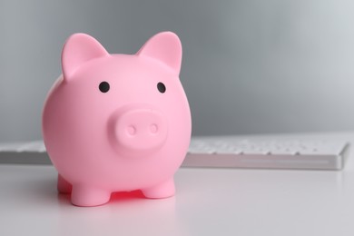 Photo of Pink piggy bank and keyboard on white table, space for text