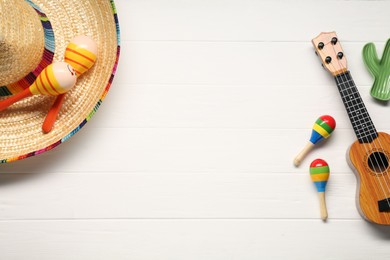 Photo of Mexican sombrero hat, maracas and guitar on white wooden background, flat lay. Space for text