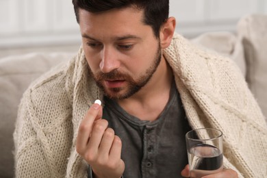 Depressed man with glass of water taking antidepressant pill on blurred background