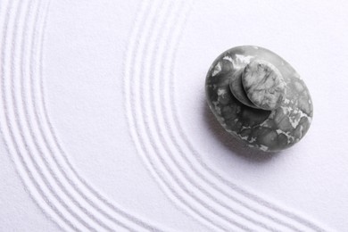 Photo of Zen garden stones on white sand with pattern, top view. Space for text