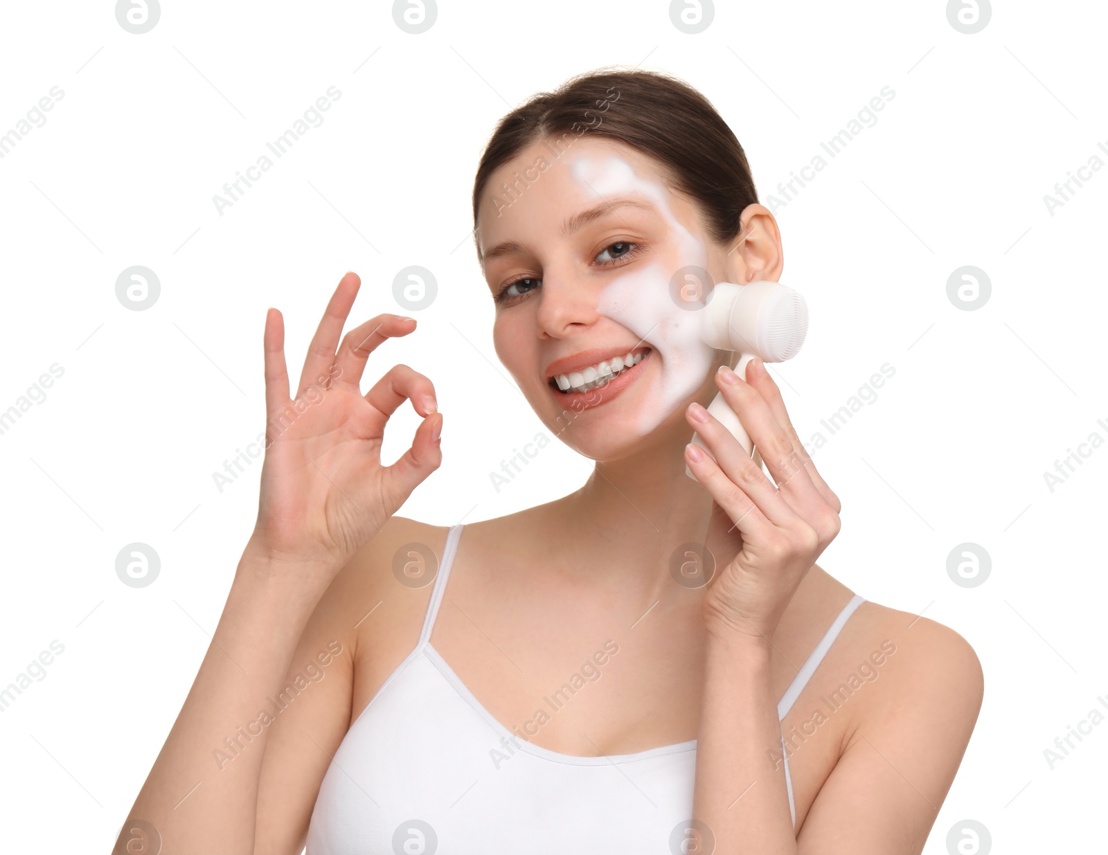 Photo of Young woman washing face with brush and cleansing foam on white background