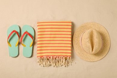 Beach towel, hat and flip flops on sand, flat lay