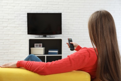 Photo of Woman changing TV channel with remote control on sofa in living room. Space for text