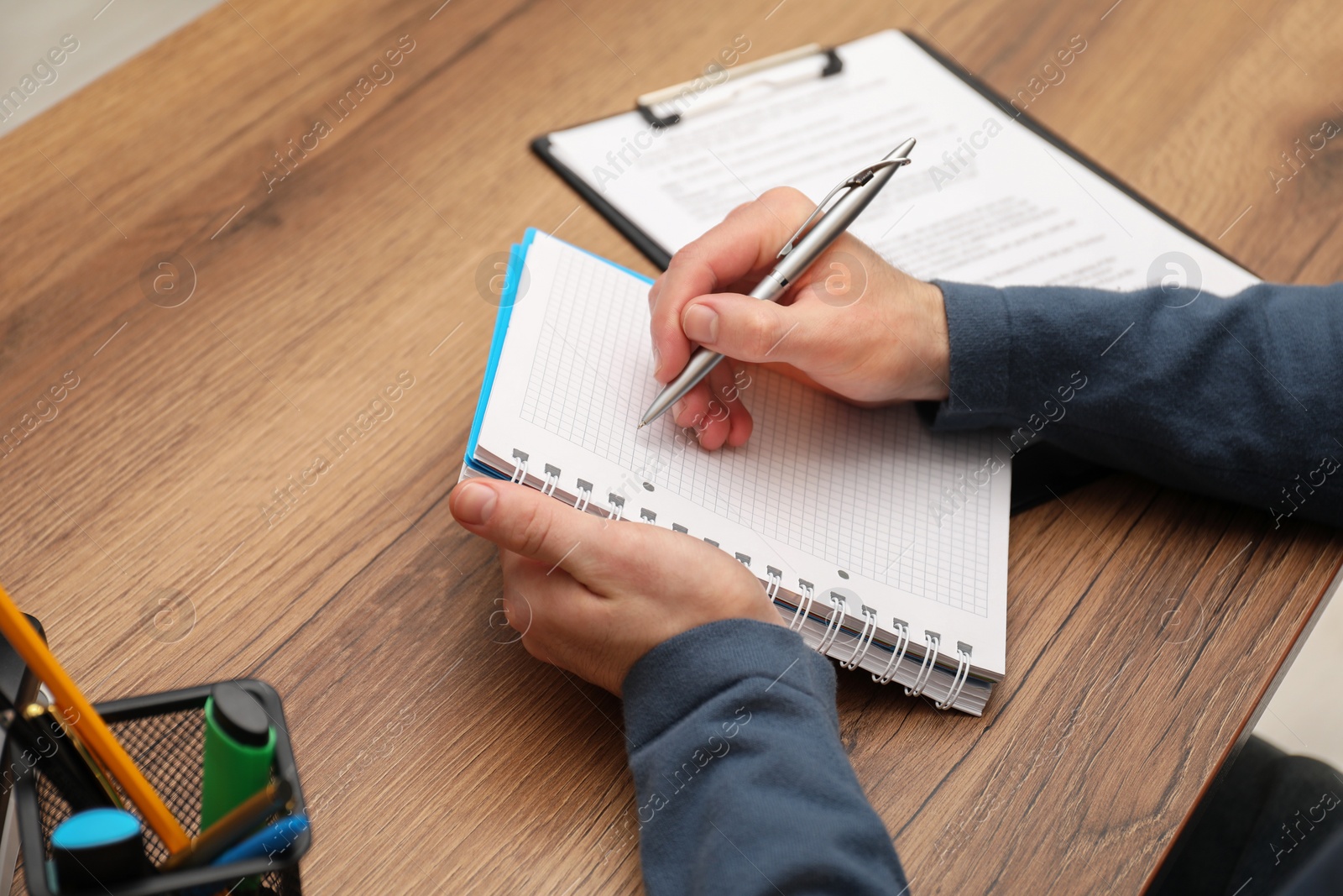 Photo of Man taking notes at wooden table, closeup