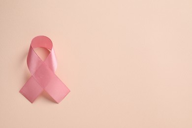 Pink ribbon on beige background, top view and space for text. Breast cancer awareness