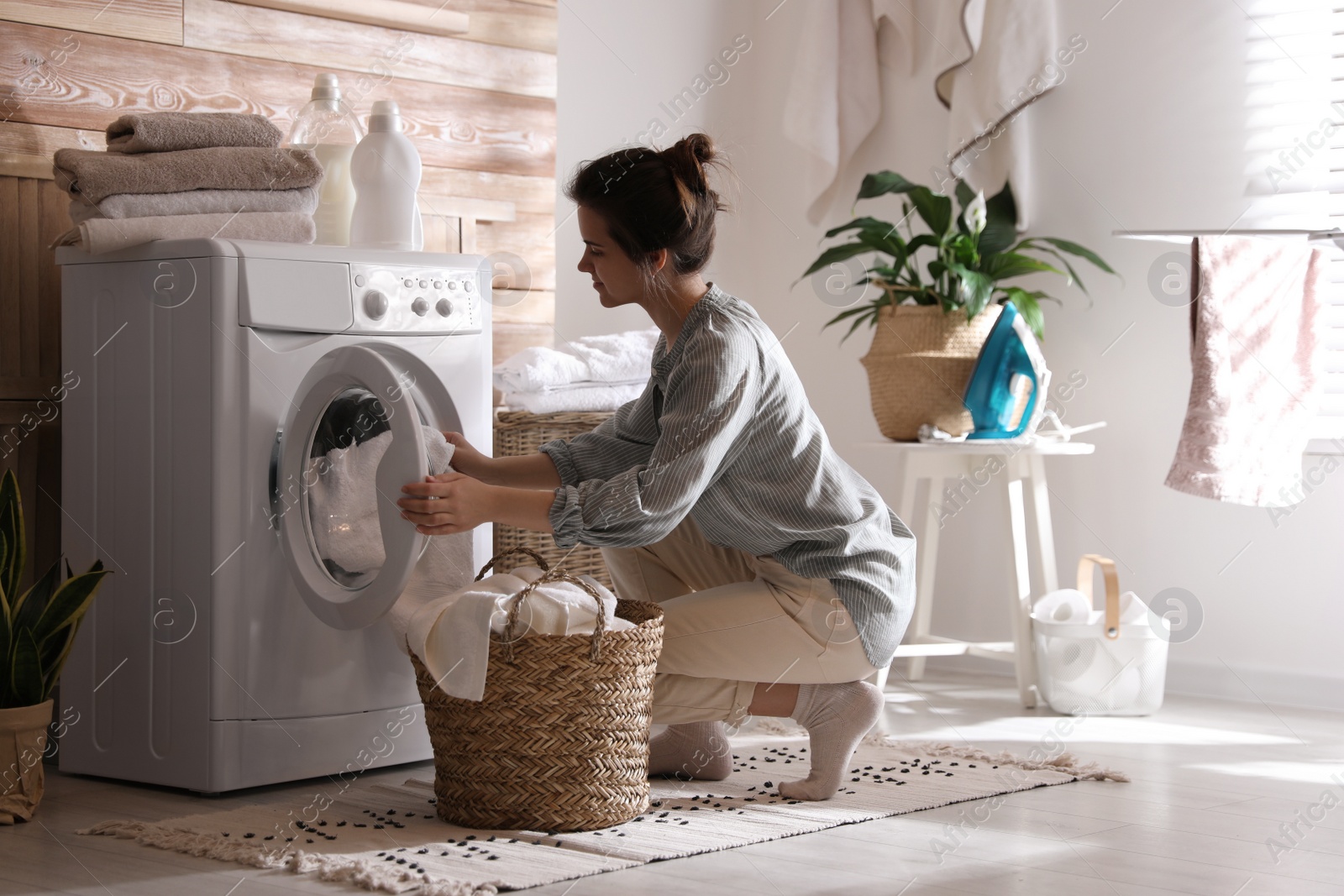 Photo of Young woman taking laundry out of washing machine at home