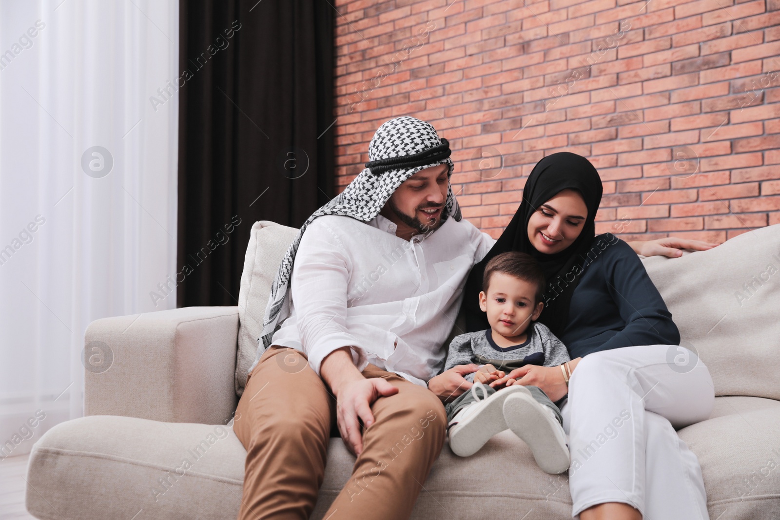 Photo of Happy Muslim family spending time together on sofa at home, space for text