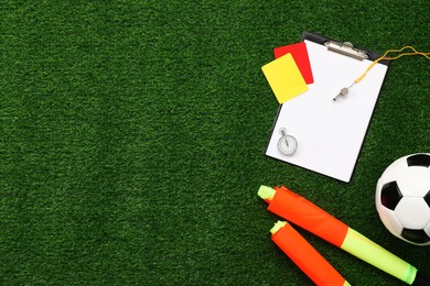 Soccer ball and different referee equipment on green grass, flat lay. Space for text