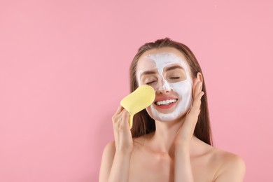 Photo of Happy young woman washing off face mask with sponge on pink background. Space for text