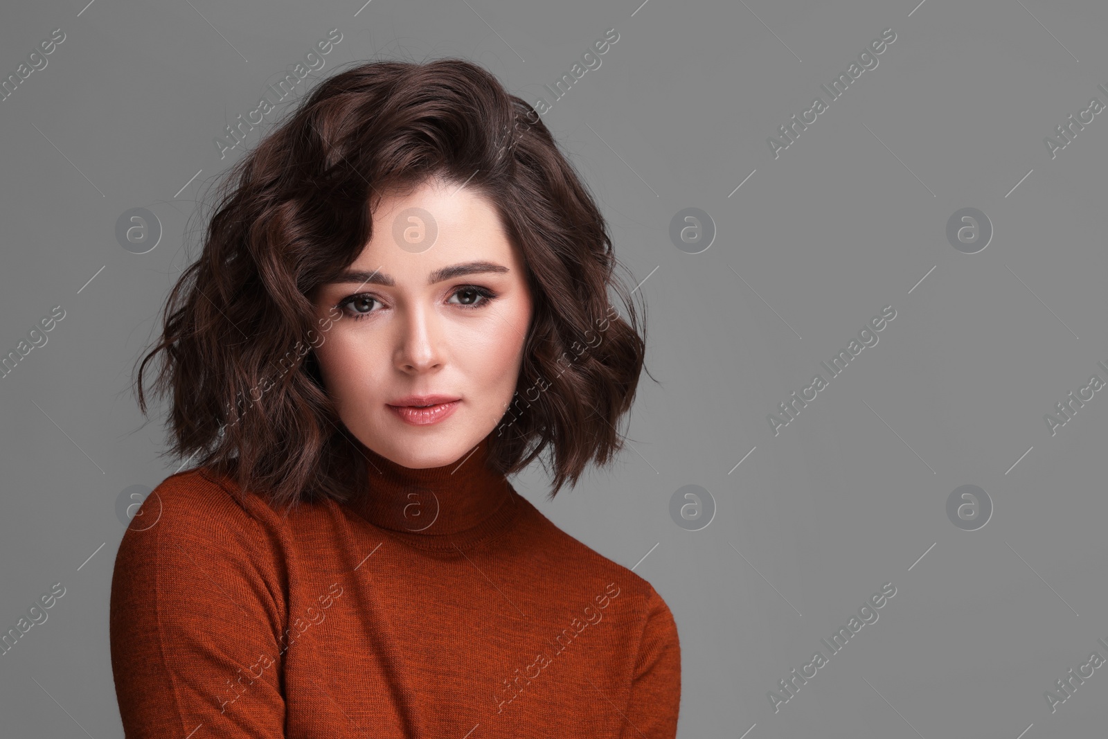 Photo of Portrait of beautiful young woman with wavy hairstyle on grey background. Space for text