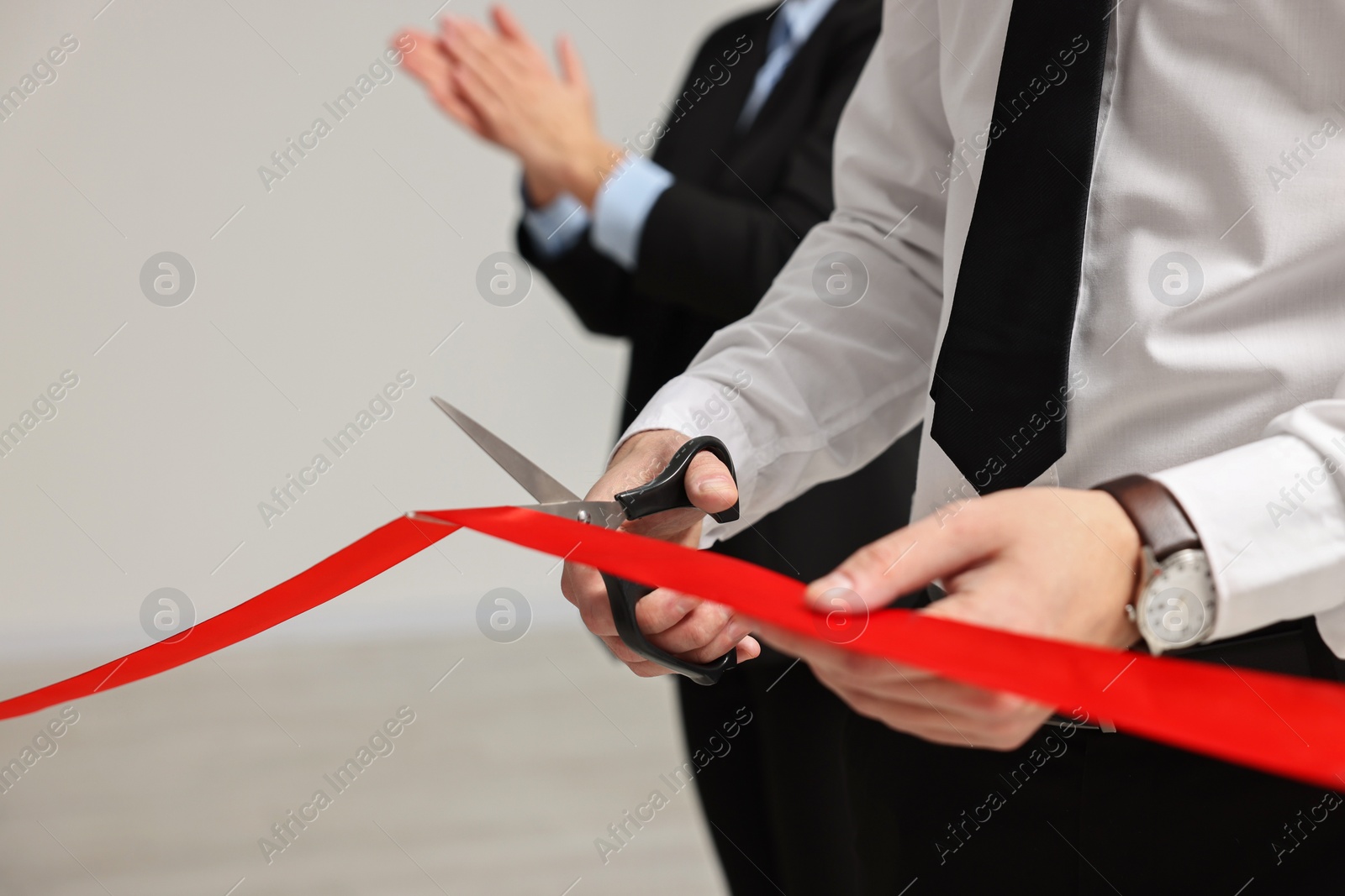 Photo of Man cutting red ribbon with scissors indoors, closeup