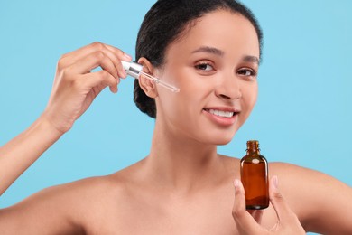 Photo of Smiling woman applying serum onto her face on light blue background