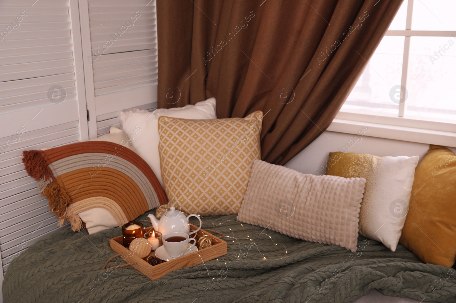 Photo of Comfortable lounge area with knitted blanket and soft pillows near window in room