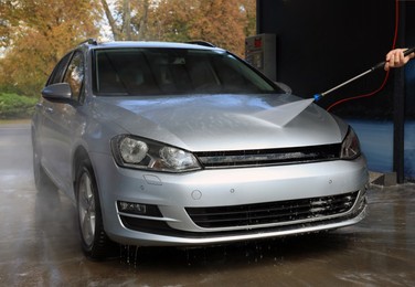 Photo of Man washing auto with high pressure water jet at outdoor car wash, closeup