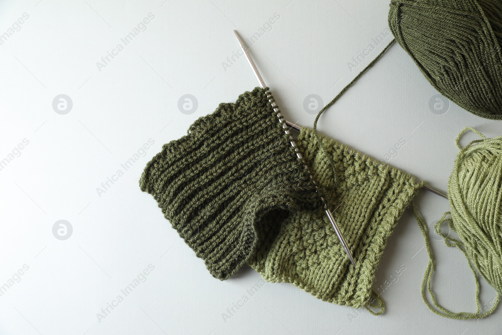 Photo of Green knitting, needles and soft yarns on light background, flat lay. Space for text