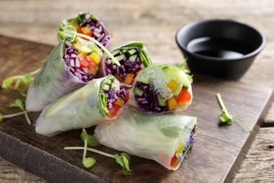 Photo of Delicious spring rolls and soy sauce on wooden table, closeup