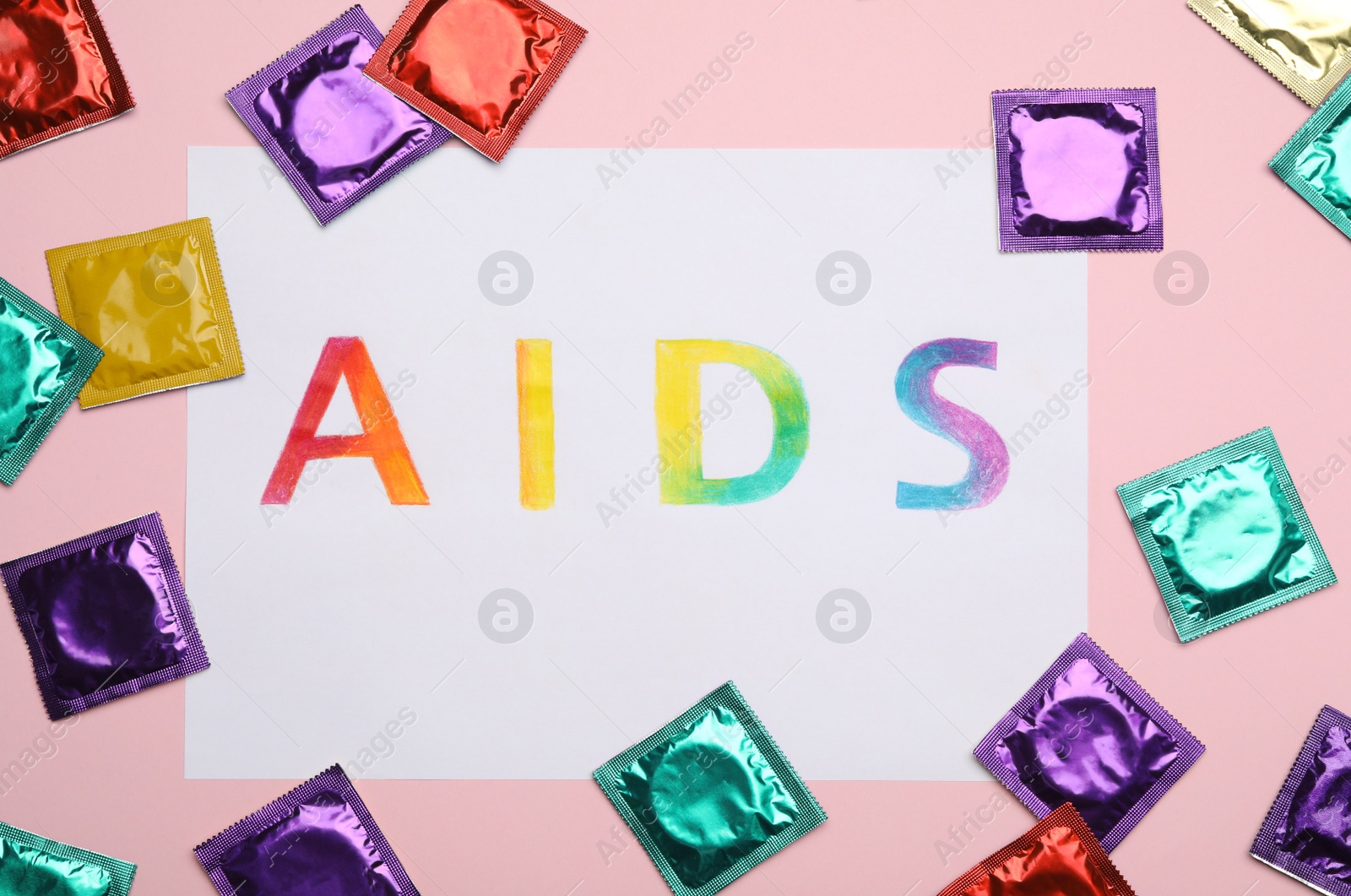 Photo of Colorful condoms and paper sheet with word AIDS on pink background, flat lay. Safe sex