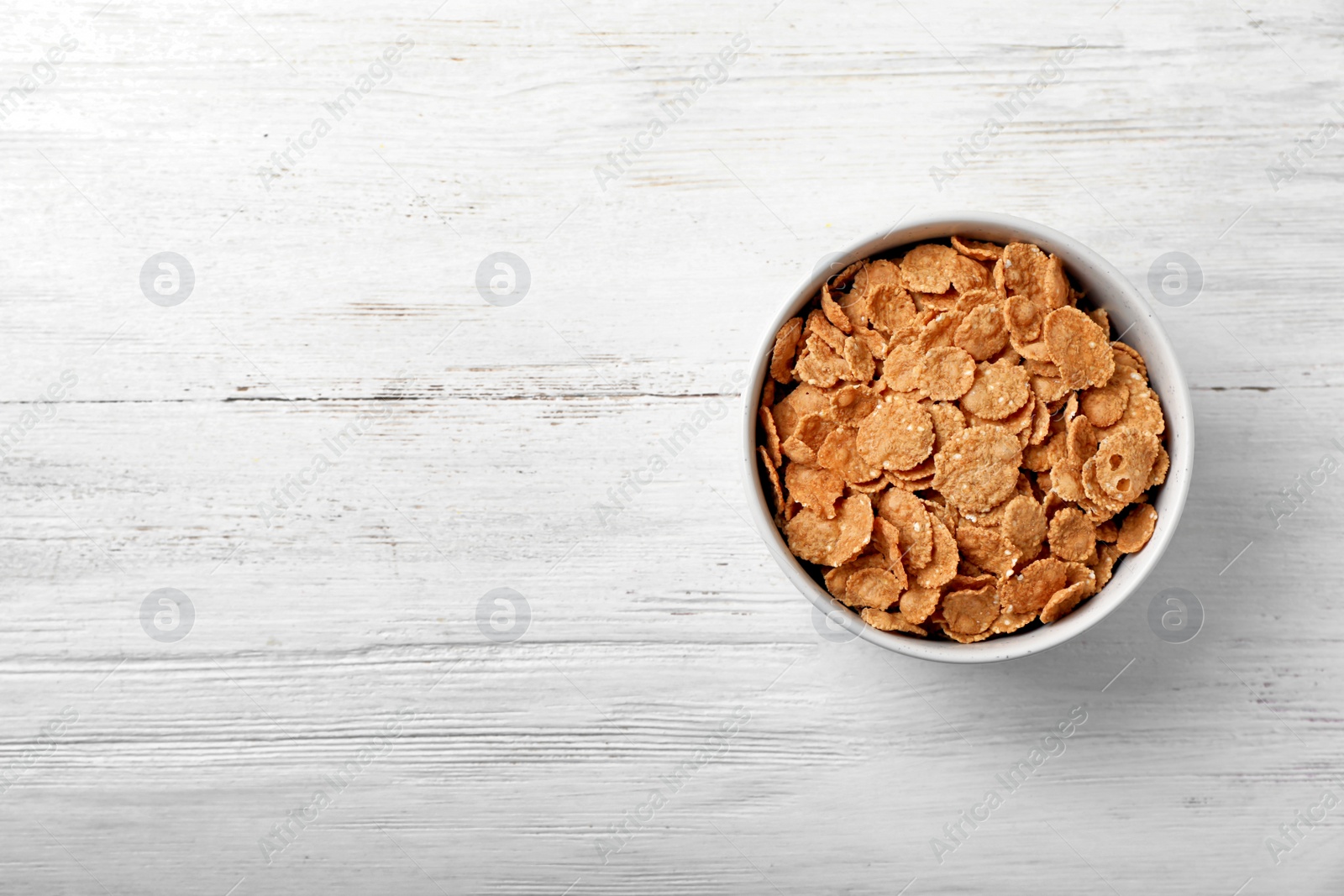 Photo of Bowl of cornflakes on light table, top view with space for text. Whole grain cereal for breakfast