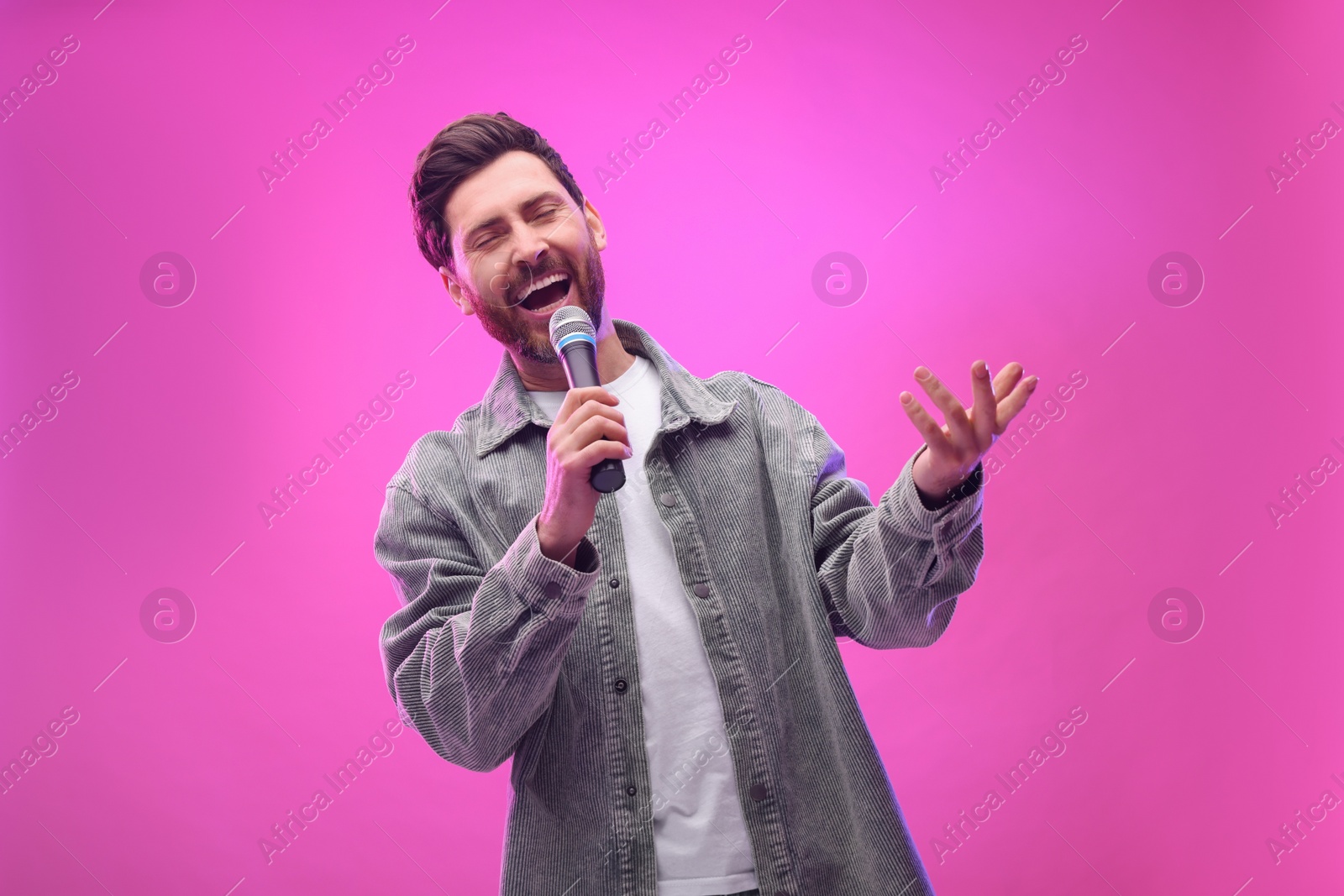 Photo of Handsome man with microphone singing on pink background