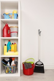 Photo of Shelving unit with detergents and cleaning tools near white wall indoors