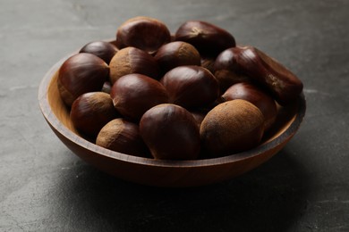 Roasted edible sweet chestnuts in bowl on grey textured table, closeup