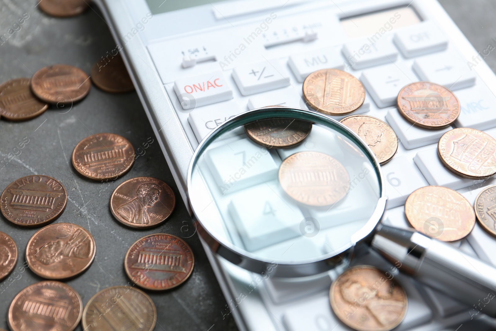 Photo of Calculator, magnifying glass and coins on grey stone table, closeup. Search concept