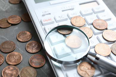 Calculator, magnifying glass and coins on grey stone table, closeup. Search concept
