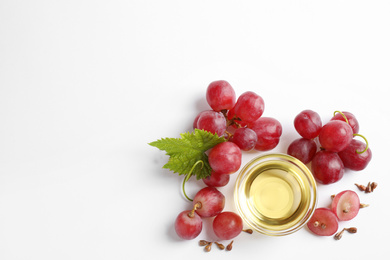 Organic red grapes, seeds and bowl of natural essential oil on white background, flat lay. Space for text