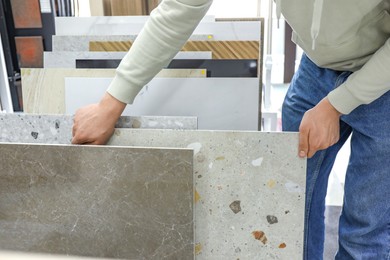 Photo of Man choosing tile among different samples in store, closeup