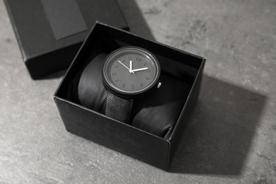 Box with stylish wrist watch on gray table. Fashion accessory