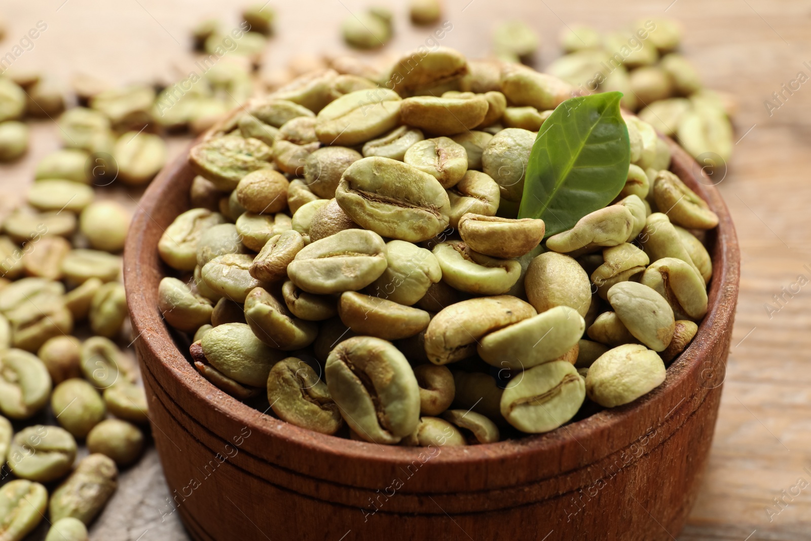 Photo of Green coffee beans and leaf on wooden table, closeup