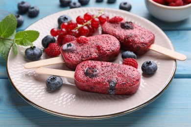Photo of Plate of tasty berry ice pops on light blue wooden table, closeup. Fruit popsicle