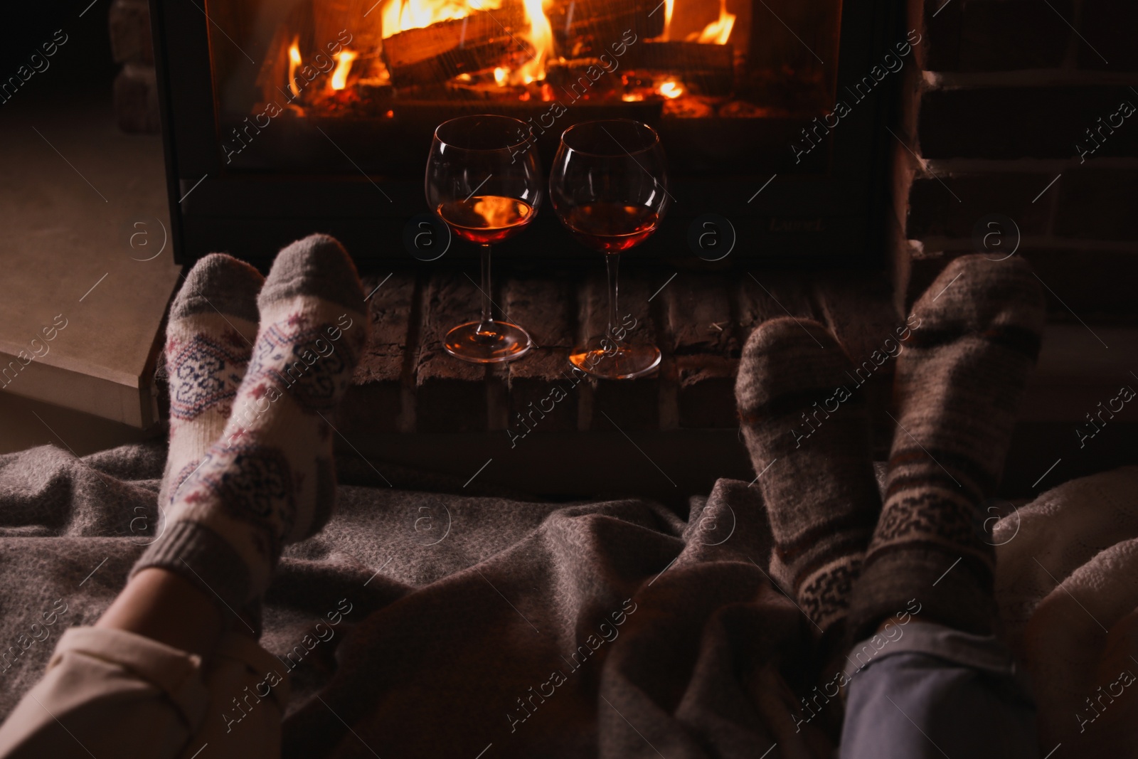 Photo of Couple and glasses of red wine near burning fireplace, closeup