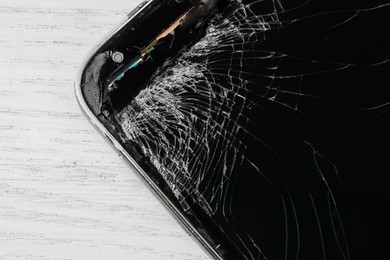 Photo of Smartphone with cracked screen on light beige wooden background, closeup. Device repair