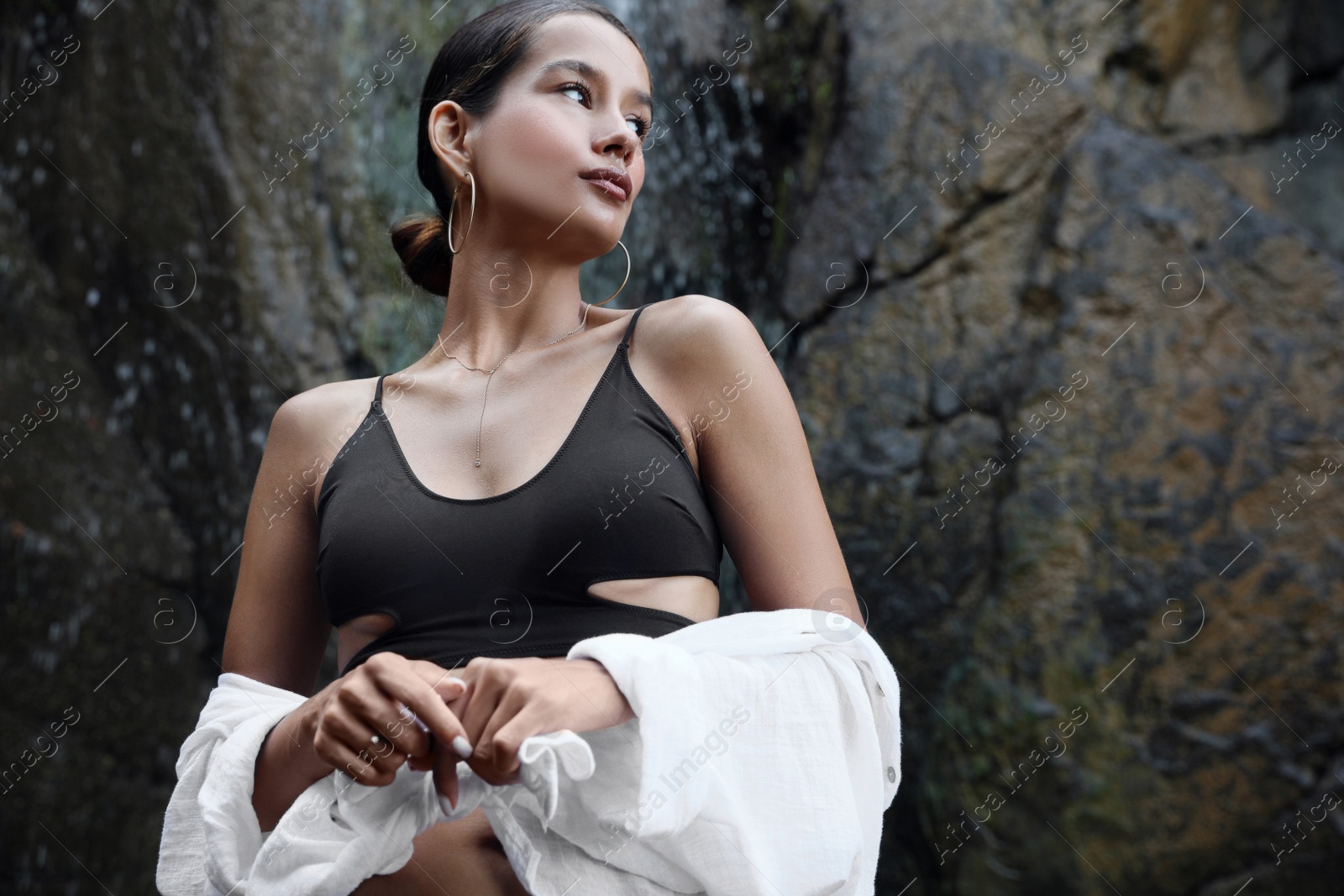 Photo of Beautiful young woman in stylish bikini near waterfall outdoors, low angle view. Space for text