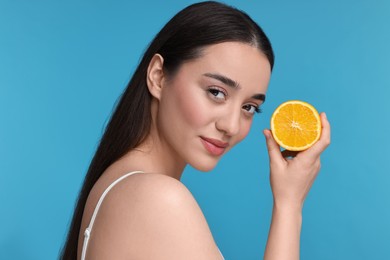 Beautiful young woman with piece of orange on light blue background