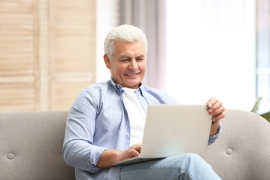 Photo of Portrait of mature man with laptop on sofa indoors