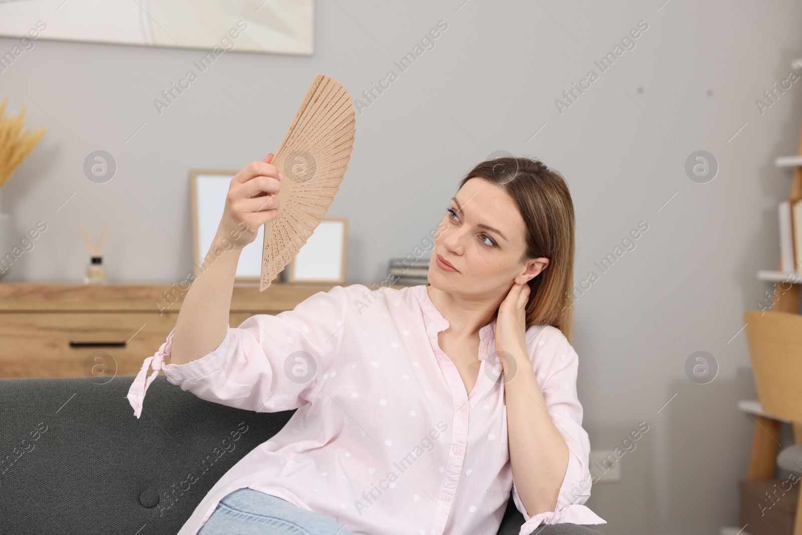 Photo of Woman waving hand fan to cool herself on sofa at home