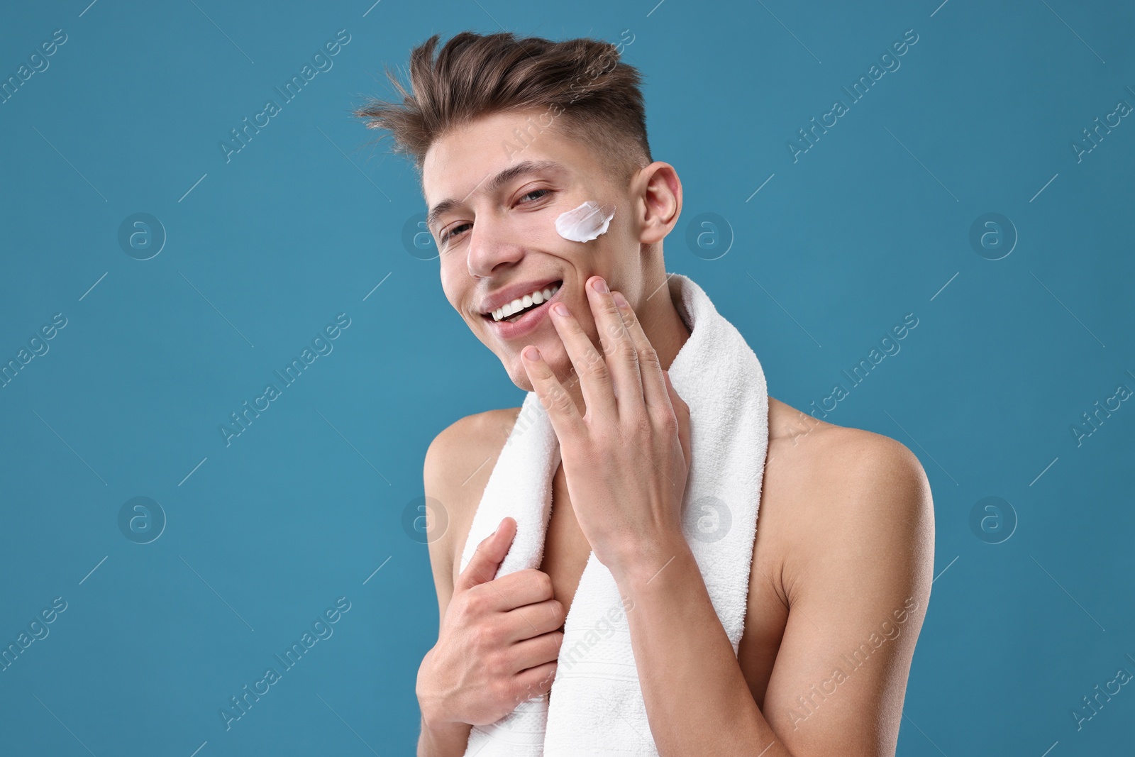 Photo of Handsome man applying moisturizing cream onto his face on blue background
