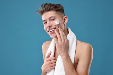 Photo of Handsome man applying moisturizing cream onto his face on blue background