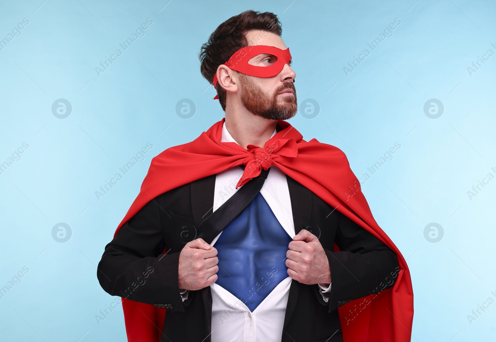 Image of Confident businessman wearing superhero costume under suit on light blue background