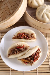 Photo of Plate with delicious gua bao (pork belly buns) and bao buns (baozi) on bamboo mat, top view
