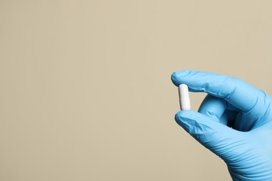 Doctor holding pill on beige background, closeup. Space for text