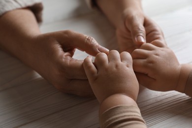 Woman holding hands with her little daughter at white wooden table, closeup