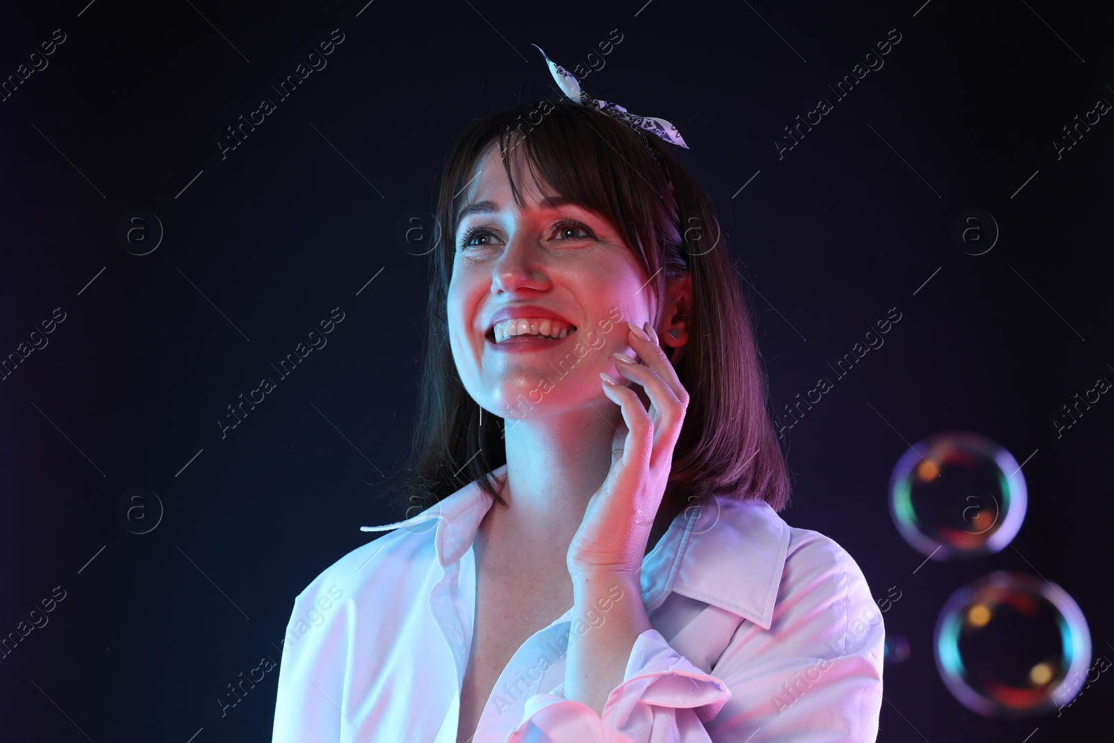 Photo of Portrait of happy woman among bubbles on dark background, space for text