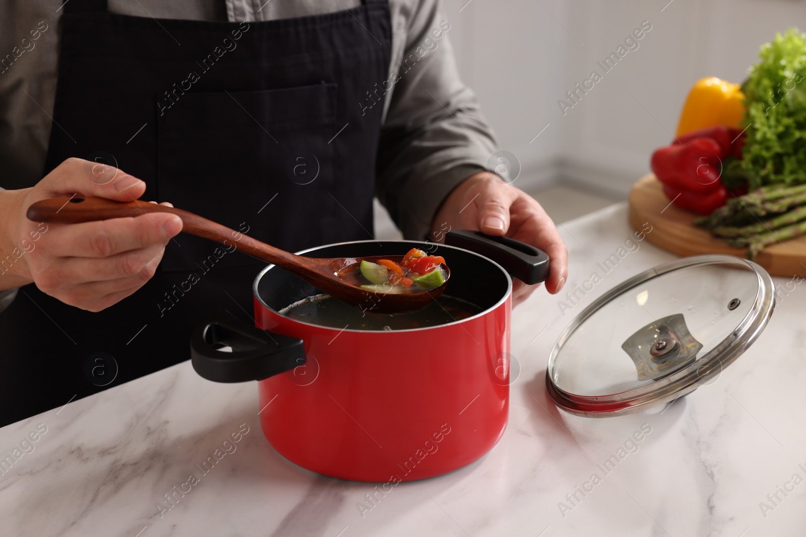 Photo of Cooking process. Man with pot of soup at white marble countertop indoors, closeup