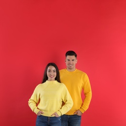 Photo of Happy couple wearing yellow warm sweaters on red background. Space for text