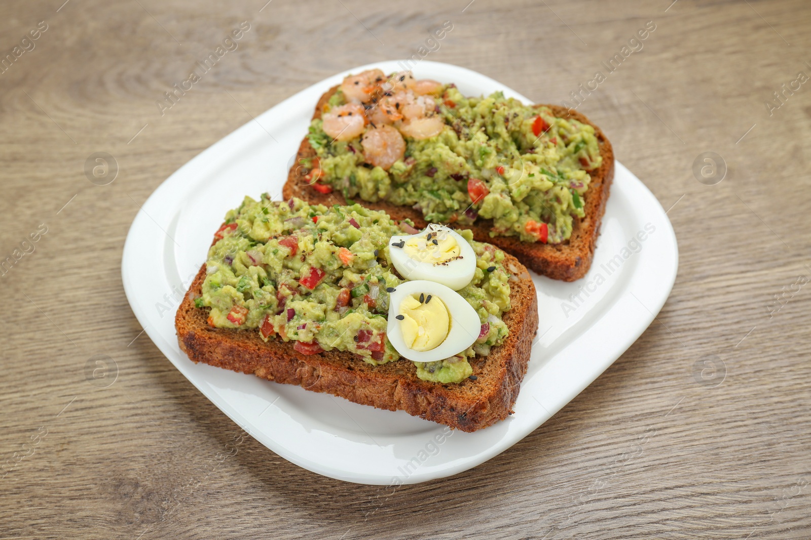 Slices of bread with tasty guacamole, eggs and shrimp on wooden table, closeup Photo of Slices of bread with tasty guacamole, eggs and shrimp on wooden table, closeup