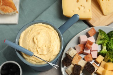 Photo of Tasty melted cheese in fondue pot, fork and snacks on table, flat lay
